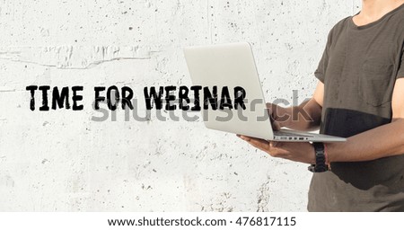 Young man using laptop and TIME FOR WEBINAR concept on wall background