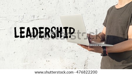 Young man using laptop and LEADERSHIP concept on wall background