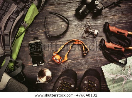 Hiking accessories set on dark wooden background:  boots, backpack, sunglasses, photo camera, map, smartphone, flashlight and others. Top view. Vintage retro effect