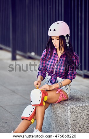 Beautiful girl puts on protective gear for rollerblading. Stylish pink skating helmet, knee pads and quad roller skate.