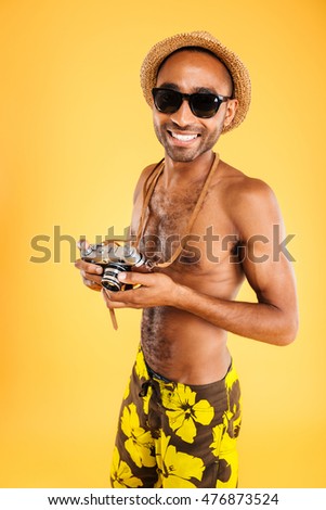 Portrait of a happy afro american man holding retro photo camera isolated on a orange background