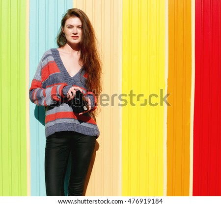 the girl in the warm sweater, black jeans posing near the colorful wall of the house on the street. pretty hipster woman having fun in the city with retro camera, making pictures