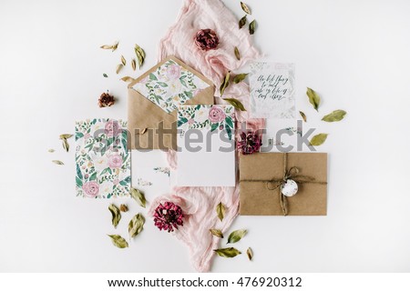 Workspace. Wedding invitation cards, craft envelopes, pink and red roses and green leaves on white background. Overhead view. Flat lay, top view