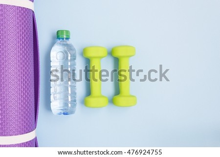 Two green dumbbells, bottle of water and yoga mat over blue background Royalty-Free Stock Photo #476924755