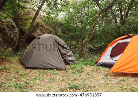 Tourist red and green tents in forest at campsite near mountain rocks. Camping place in the meadow on nature in summer. Adventure travel active lifestyle outdoor background. Family time holidays.