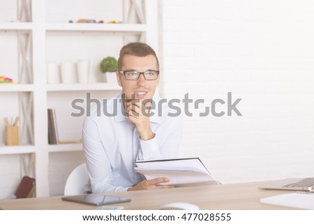 Young businessman with paperwork in hand thinking at office desk with objects
