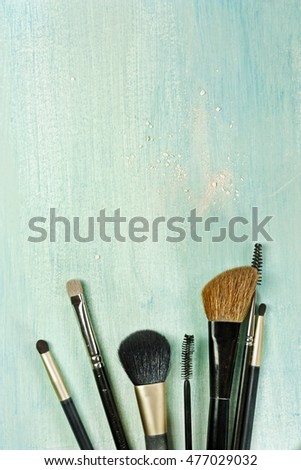 Makeup brushes on a teal blue background, with traces of powder on it; a vertical template for a makeup artist's business card or flyer design; with plenty of copyspace