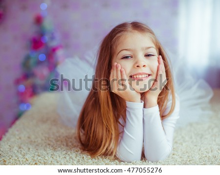 Little girl dressed like a dances holds her face while lying on the carpet