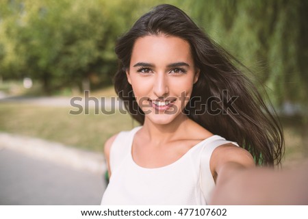 Self portrait of beautiful young brunette smiling woman on nature and sky background in the park. Travel. Selfie. Instagram