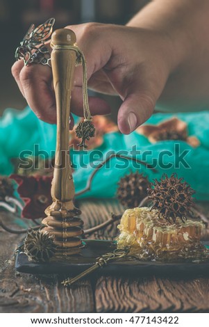 Woman hand with the silver wasp ring holding a honey spoon over honeycombs and nuts.