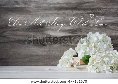 Background with motivation quote with white hydrangea bouquet and books on the vintage table. Wedding decoration with text. Do all things with love.
