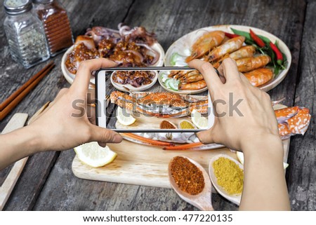 Girl taking pictures on mobile smart phone a jumbo crab and spices herb on dark background