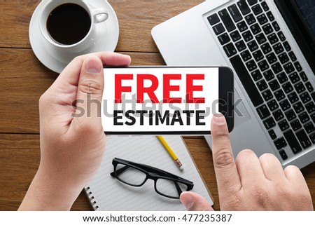 FREE ESTIMATE message on hand holding to touch a phone, top view, table computer coffee and book