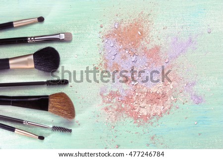 Makeup brushes on a teal blue background, with traces of powder and blush on it; a horizontal template for a makeup artist's business card or flyer design; with plenty of copyspace