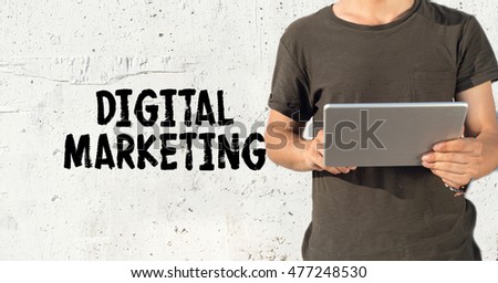 Young man using tablet pc and DIGITAL MARKETING concept on wall background