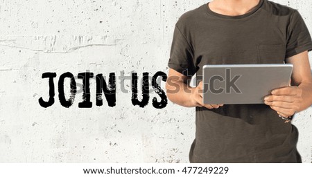 Young man using tablet pc and JOIN US concept on wall background