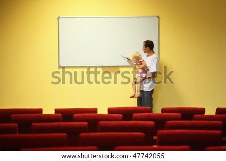 father and little girl in empty presentation hall. little girl is drawing on a board