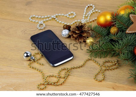 Festive greetings on-line. Xmas . SMS. modern technologies.Modern Christmas present. Smartphone and branches of a Christmas tree on a wooden background.