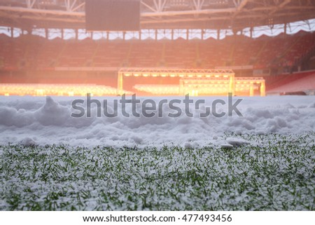 Closeup view of snow on green field in football stadium with lamps
