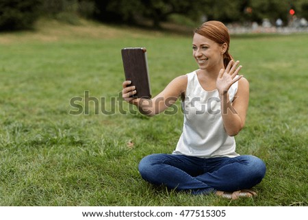 Woman in a park video chatting on tablet computer