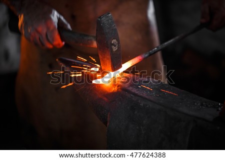 The blacksmith manually forging the molten metal on the anvil in smithy with spark fireworks Royalty-Free Stock Photo #477624388