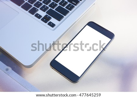 Smartphone on a table next to a laptop. Blank display replaceable with needed design.Vertical mockup