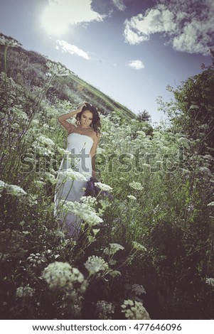 Beatiful young woman in white dress running across the blossom field