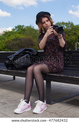 Girl with the digital camera sitting on a bench and looking at the display