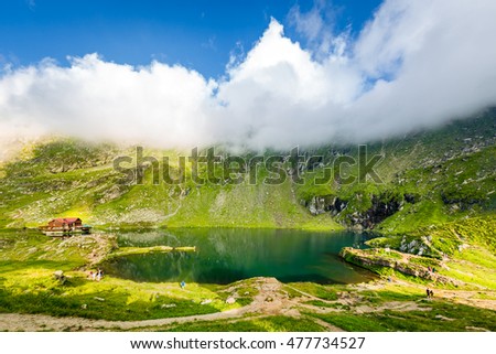 Balea lake and chalet in Fagaras mountains, Romania. Unidentifiable tourists enjoy the scenery. Royalty-Free Stock Photo #477734527