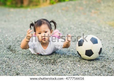 1 year old baby playing soccer football and she falls down on the ground. Picture for concept of child safety and injury prevention.