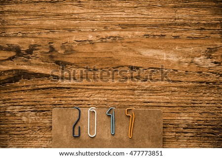 Happy new year 2017 made from new plastic paper clips, lie on brown paper and wooden background, retro style