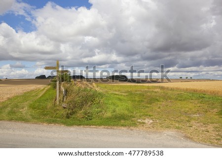 A wooden signpost in the agricultural countryside of the Yorkshire wolds under a blue cloudy sky in summertime