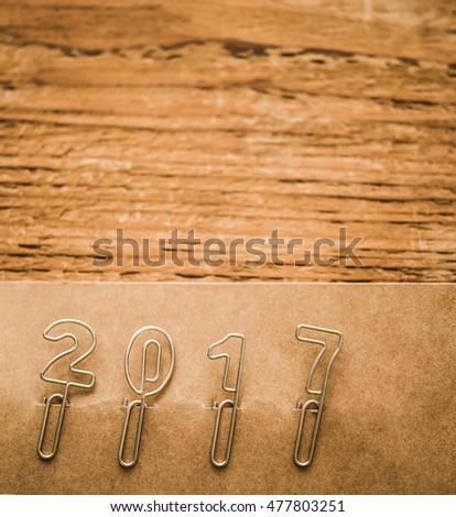 Happy new year 2017 made from new metal paper clips, lie on brown paper and wooden background, retro style