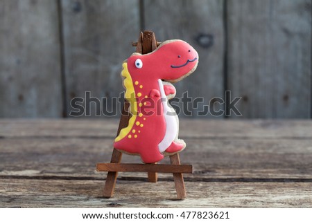 Homemade gingerbread cookie in the shape of red dinosaur on a wooden background. Space for text and selective focus.