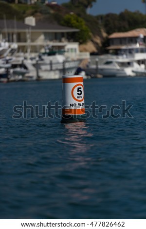 5 MPH No Wake Buoy floating in a harbor with orange warning tape and sea moss on the bottom