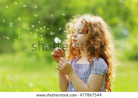 Little curly girl blowing dandelion. Royalty-Free Stock Photo #477867544