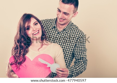 Smiling young couple holding paper key to heart sign love symbol. Loving husband and wife dreaming about new home. Instagram filtered.