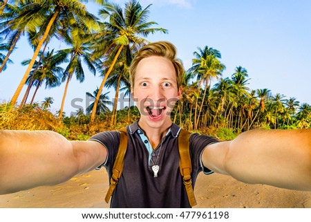Young happy man taking selfie using front camera on a tropical beach