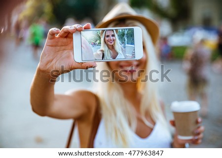 Young smiling cheerful blonde girl making selfie while standing on the street