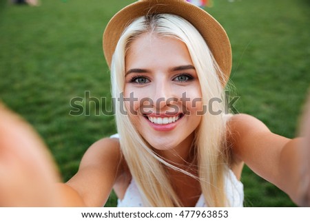Young smiling cheerful blonde girl in hat making selfie while standing on the street