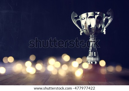 low key image of trophy over wooden table and dark background, with abstract shiny lights Royalty-Free Stock Photo #477977422