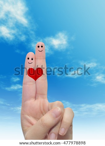 Concept or conceptual human or female hands with two fingers painted with a red heart and smiley faces over cloud blue sky background for valentine, romantic, love, couple, young, family or wedding