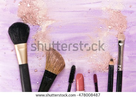 Makeup brushes, lipstick and pencil on a light purple background, with traces of powder and blush on it; a horizontal template for a makeup artist's business card or flyer design; with copyspace