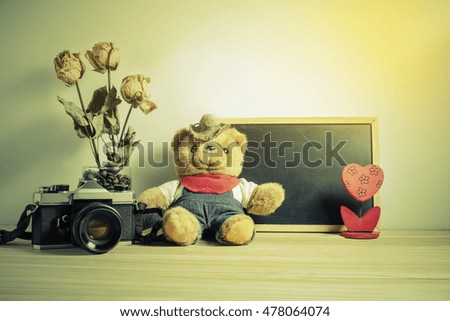 Old vintage camera and teddy bear on wooden background with small blank blackboard. image at adjustment color sepia style.
