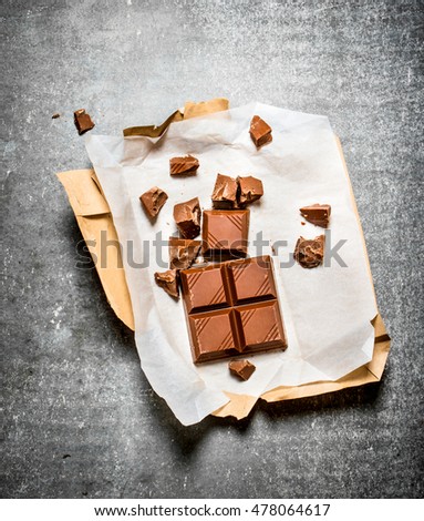 Milk chocolate in paper. On the stone table.