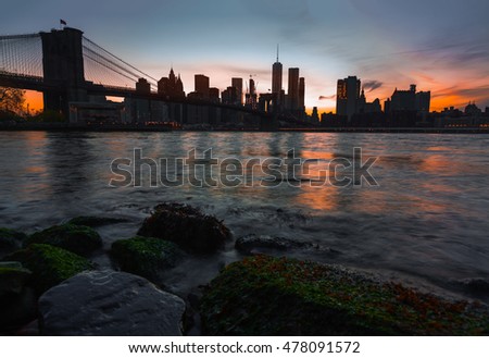 Manhattan skyline with Brooklyn Bridge in the evening. Rocks and stones on the shore of the East River