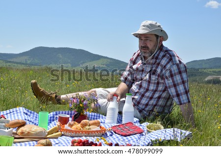 Man with hat on picnic on sunny day with hills of Zlatibor Mountain in background