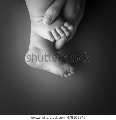 Newborn baby legs with mother hand isolated on grey background
