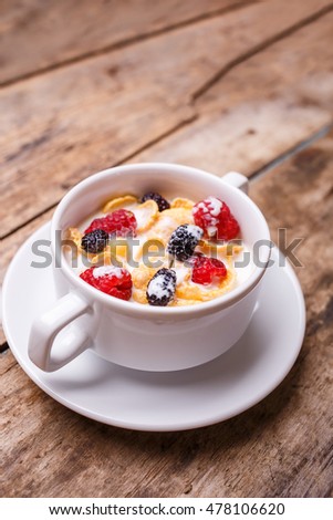 Breakfast menu background. Corn flakes with berries and milk in white bowl on wood background