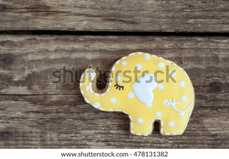 Homemade gingerbread cookie in the shape of yellow elephant with polka dots on a wooden background. Space for text and selective focus.